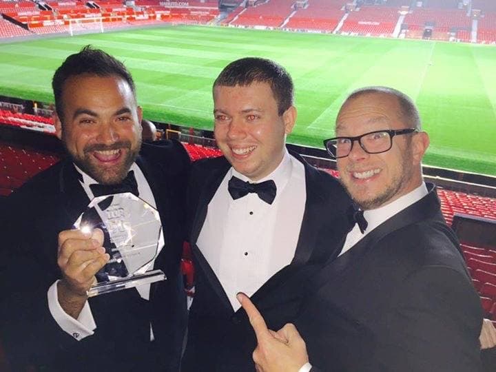 Mark Kirby and two colleagues in black tie holding a Top 50 award at Old Trafford